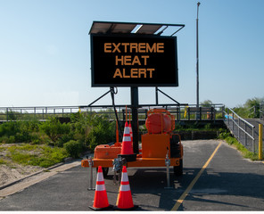 Electronic mobile sign that says Excessive Heat Alert. The sign is on a deserted street by the entrance to the boardwalk by the beach