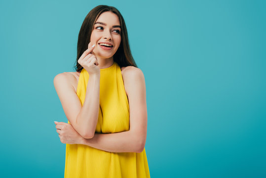 happy brunette girl in yellow dress snapping fingers isolated on turquoise