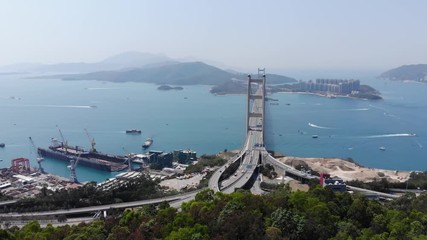 Aerial camera fly over green trees towards Tsing Ma bridge and industrial shore on reclaimed land at west side of Tsing Yi island. Wide angle perspective from above, Lantau Link interchange ahead