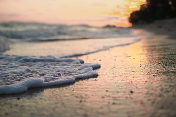 Fototapeta na wymiar close up sea foam on sandy beach, sunset over beach.