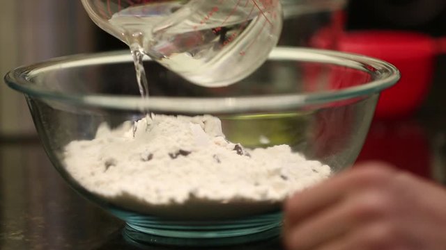 Close up of man pouring water and oil into mixing bowl