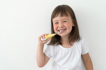 A girl in a white T-shirt brushes her teeth with an electric brush. Cute girl on a light background...