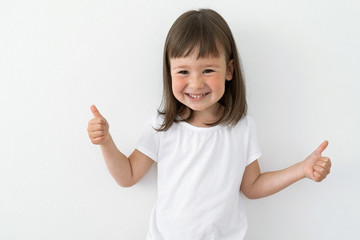 Joyful child in a white T-shirt on a light background. Cute girl smiles and shows class