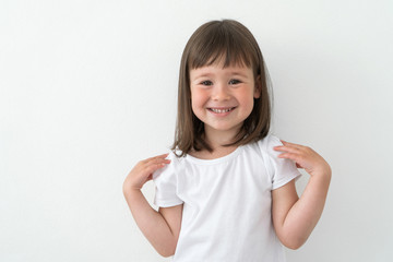 Joyful child in a white T-shirt on a light background. Cute girl smiles and does exercises.