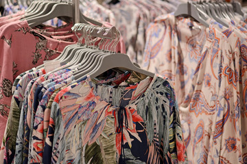 Naklejka na ściany i meble Clothes on hangers in store. Womens floral blouses hang on clothing rack. Shopping time concept
