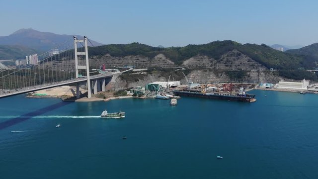 Tsing Yi island aerial view from Ma Wan Channel, Tsing Ma bridge on left. Industrial docks on reclaimed land, cut hills for highway interchange and green forested mounts range