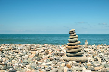 Cairn on a pebble beach against the background of the sea and the second cairn on a sunny day. Travel and Vacation Concept