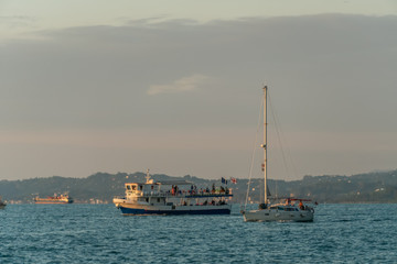 Small pleasure tourist boat sailing from the port for a cruise off the coast on a summer evening against the mountains, Batumi