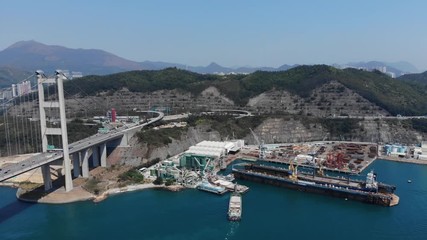 Aerial shot of Tsing Yi island at connection with Tsing Ma bridge, industrial shore and dry dock, large highway interchange. Cut land of hills, some buildings of factory at dock yards
