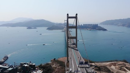 Lengthwise aerial perspective of large Tsing Ma suspension bridge at Hong Kong, Lantau Link highway part. Sea channel and islands seen ahead, some boats on water, easy traffic on road