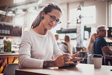 Young pretty woman with tattooes on her hands is enjoying her time at food court with her sketching pad.