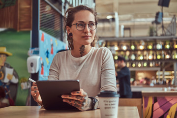 Attractive creative girl with tattooes on her hands is sitting at cafe while sketching in her...