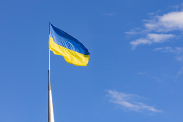 Waving flag of Ukraine on the street flagpole with blue cloudy sky on background. Ukrainian country symbol