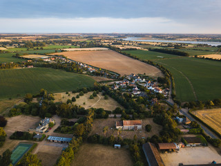 Aerial view of a small traditional village in the Suffolk countryside. The village is surrounded by farm fields growing different crops