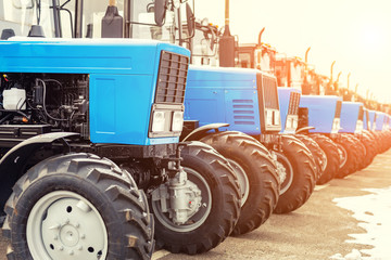 Many different tractors standing in row at agricultural fair for sale outdoors.Equipment for...