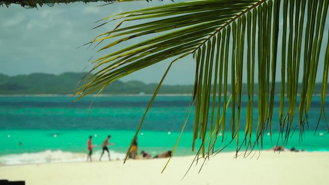 Tropical beach with tourists and clear blue sea through palm branches. Summer and travel vacation concept. Philippines