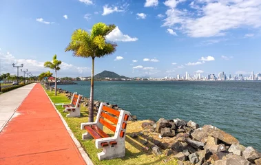 Fotobehang De Amador Causeway-weg, de beroemde bloeiende promenade en toeristische attractie van Panama City, bezaaid met parkbanken en palmbomen, met de skyline van het verre stadscentrum aan de horizon © Autumn Sky