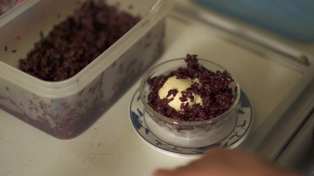 Close up front angle shot of a chef topping up of black rice to the ice cream bowl and a  paper parasol.