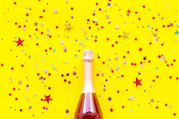 Party with champagne bottle and colorful party streamers on yellow background top view pattern