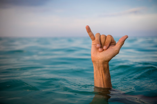 Hand of surfer making shaka (hang loose) sign in tropical blue waters