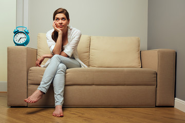 Woman sitting on sofa with alarm clock wait