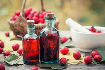 Mortar of hawthorn berries, two tincture or infusion bottles and basket of thorn apples on wooden...