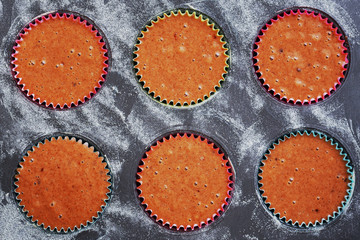 Top view of a baking tray for muffins with six colorful paper baskets filled with raw dough.
