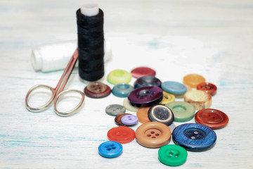 colored sewing buttons black and white threads and scissor on rustic white table