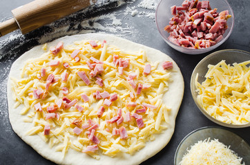 Rolled dough, baking flour, pizza filling and rolling pin on a dark blackboard.
