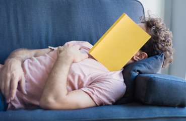 man sleep on sofa with book cover his face