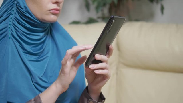 beautiful muslim woman in blue hijab using a mobile phone sitting on a sofa