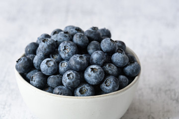 Close up of fresh blueberries in a white ceramic bowl on a light gray background