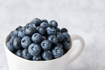 Close up of fresh blueberries in a white ceramic cup on a light gray background