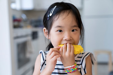 Happy cute little Asian girl eating mango with funny face
