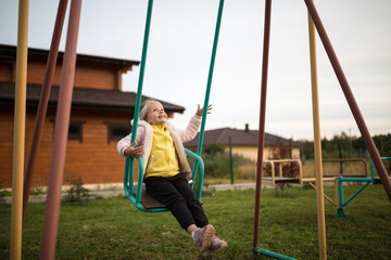 Adorable laughing little girl on swing in summer day. Happy children day concept. Kid playing outdoor on backyard