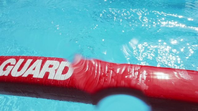 Red lifeguard float being thrown into a swimming pool. The bright rescue floatation device lands on the water, splashing drops onto the lens. Slow motion shot depicts search and rescue & saving lives.