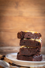 Brownie cake with almond slices stacked many layers placed on white plate, paper and wood table there are spoon and currant placed around.