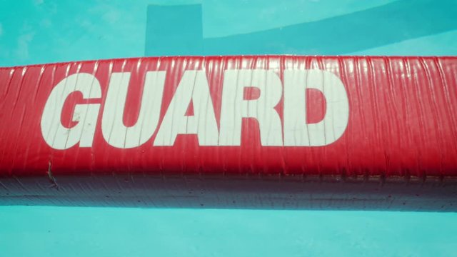 Red lifeguard float on the surface of a public swimming pool. Vibrant life preserver says "guard" in bold letters. The lifeguarding equipment is used in life-saving rescues at water parks. 