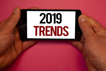 Conceptual hand writing showing 2019 Trends. Business photo showcasing New year developments in fashion Changes Innovations ModernMan hold holding cell phone white screen black red letters