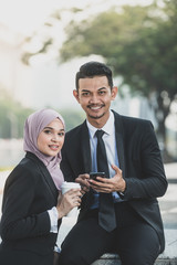 Muslim Businessman and businesswoman partner discussing using smartphone connection for work. Outdoor Setting.