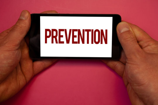 Conceptual hand writing showing Prevention. Business photo showcasing Stopping something from happening Healthcare ProtectionMan hold holding cell phone white screen black red letters pink background