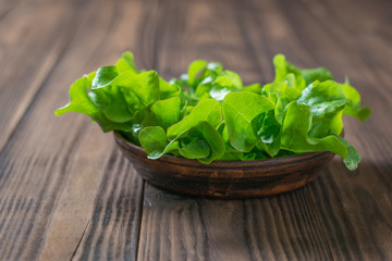 Fresh lettuce leaves in a clay bowl on a wooden table.