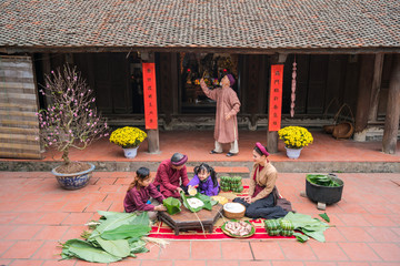 Vietnamese family members making Banh Chung together on old-styled house yard. Chung cake is a very...