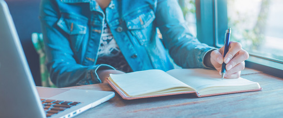 Woman hand is writing on notebook with a pen in the office.Web banner.