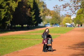 Mom walks with a stroller. A young mother enjoys the gardens when her little child is resting in her pram.
