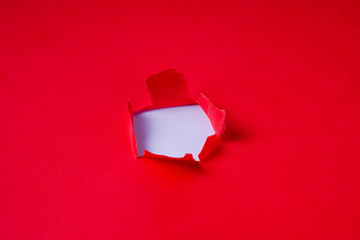 Torn red coloured paper on white background with closeup hole in the sheet of paper. Background concept with copy space.