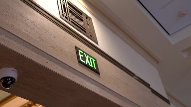 This panning video shows a glowing green exit sign and security cameras.