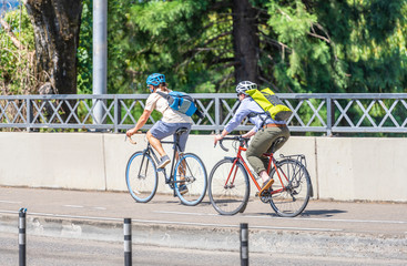 Woman and a man ride bicycles one after another along the path on the bridge along the roadway