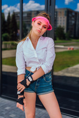 Portrait of an emotional girl in a pink cap visor and protective gloves for rollerblades and...