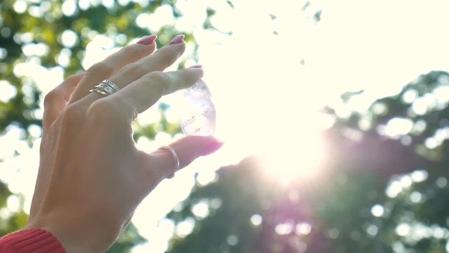 Female hand with transparent amethyst quartz yoni egg for vumfit, imbuilding or meditation. Shining crystal egg in hands on sky and sunrise background outdoors. Womens health concept.